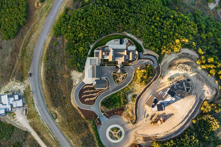 Expansive residential property featuring a multi-level structure, paved driveways, a landscaped circular entry, and surrounding natural terrain