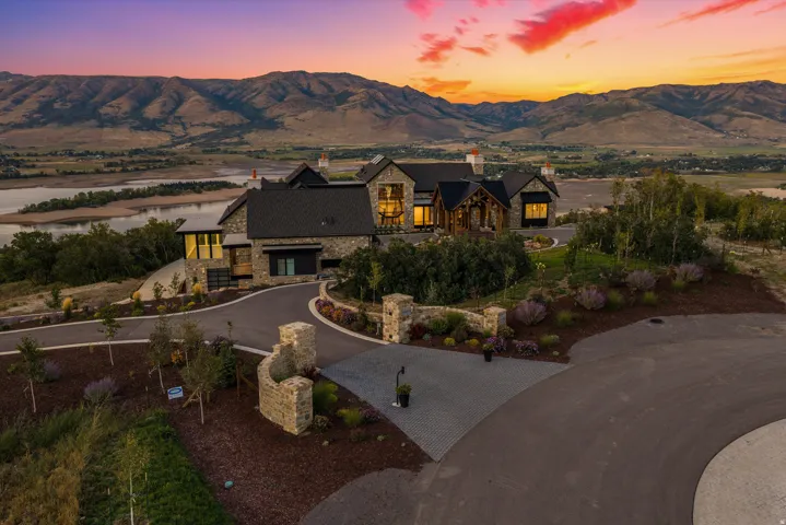 Stone exterior with multiple gables, extensive landscaping, paved driveways, and a mountain backdrop