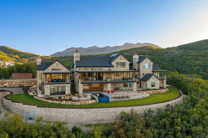 Stone-clad exterior with multiple balconies, a stone retaining wall, and a sloped roof