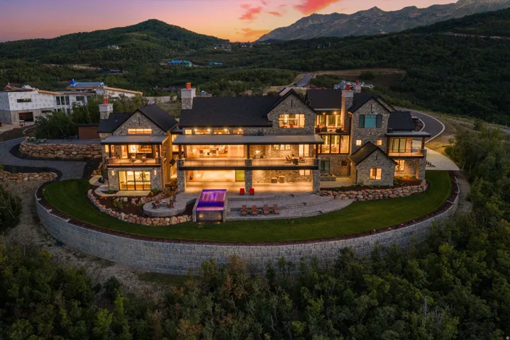 Stone exterior with multiple balconies, expansive outdoor patio, extensive landscaping, and a terraced lawn