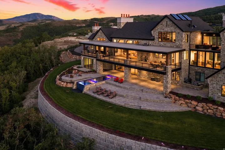 Stone exterior with multiple balconies, a multi-level patio, an infinity-edge pool, and a retaining wall