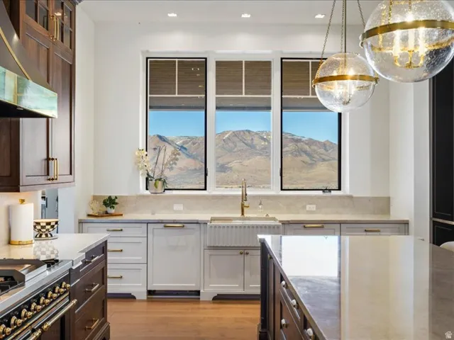 Kitchen with dual tone cabinets, glass insert cabinets, light stone counters, stainless steel stove, and light wood-type flooring