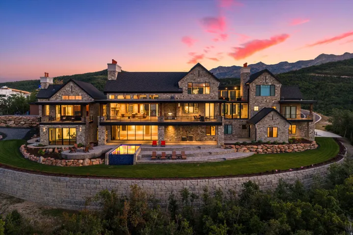 Multi-level stone exterior with expansive balconies, a terraced lawn, an infinity-edge pool, and surrounding mountainous terrain