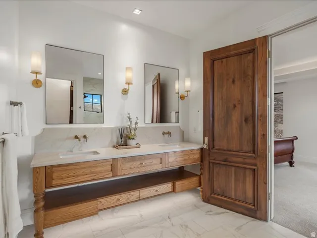 Bathroom featuring double vanity, light marble finish flooring, and backsplash