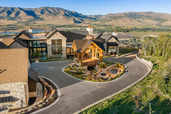 Stone exterior with prominent gabled roofs, a large paved circular driveway, and a timber-framed entry