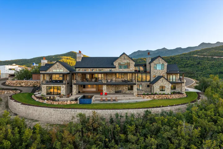 Stone exterior with multiple balconies, expansive glass panels, and a terraced lawn
