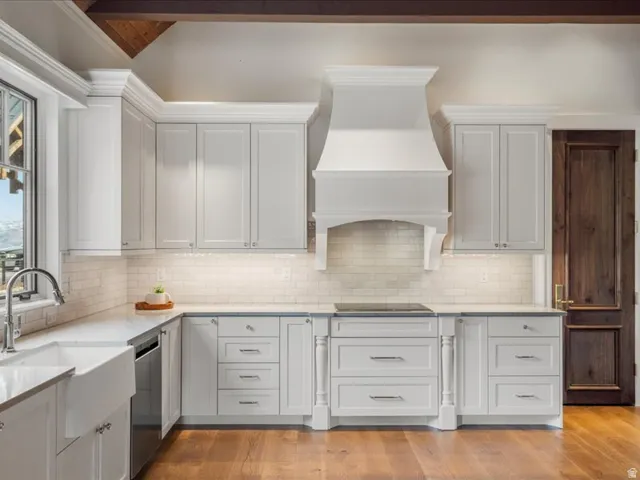 Kitchen with light stone counters, light wood-style floors, stainless steel dishwasher, white cabinets, and lofted ceiling with beams