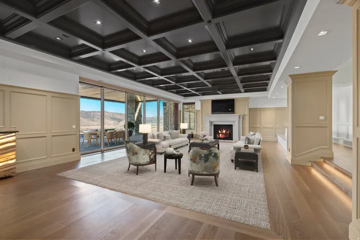 Living room with a decorative wall, coffered ceiling, light wood-style flooring, a warm lit fireplace, and recessed lighting