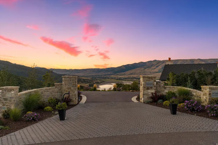 Paver driveway with stone pillar and wall entry, framed by established landscaping