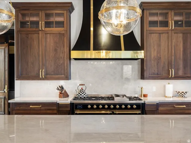 Kitchen featuring glass fronted cabinets, decorative backsplash, range with two ovens, pendant lighting, and light stone countertops