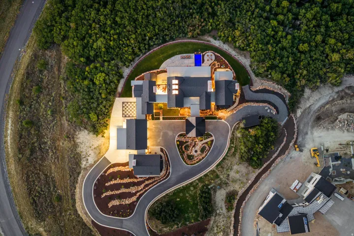 Expansive property featuring a multi-level structure with multiple dark-toned roofs, a landscaped circular drive, a checkered patio, a blue-tiled pool, and extensive surrounding foliage