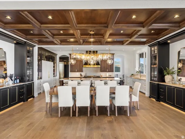 Kitchen with arched walkways, a large island with sink, coffered ceiling, glass fronted cabinets, and decorative light fixtures