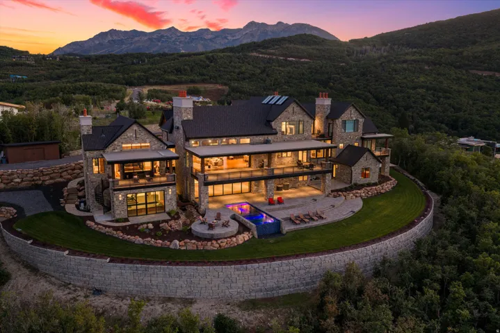Stone-clad exterior with multiple balconies, an integrated swimming pool, and a manicured lawn