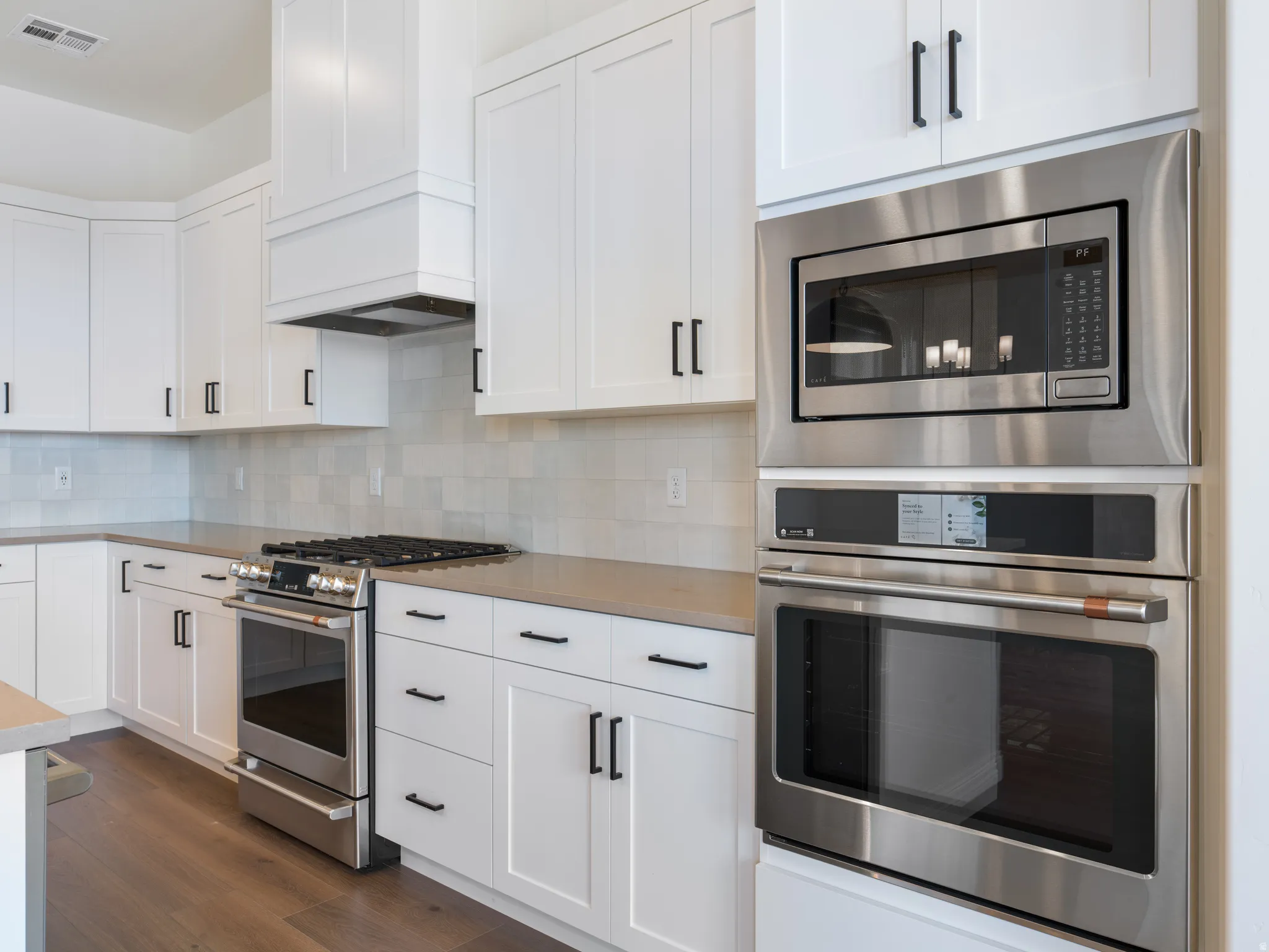 Modern kitchen featuring white cabinetry, stainless steel appliances, light-toned countertops, a tile backsplash, and wood-finish flooring