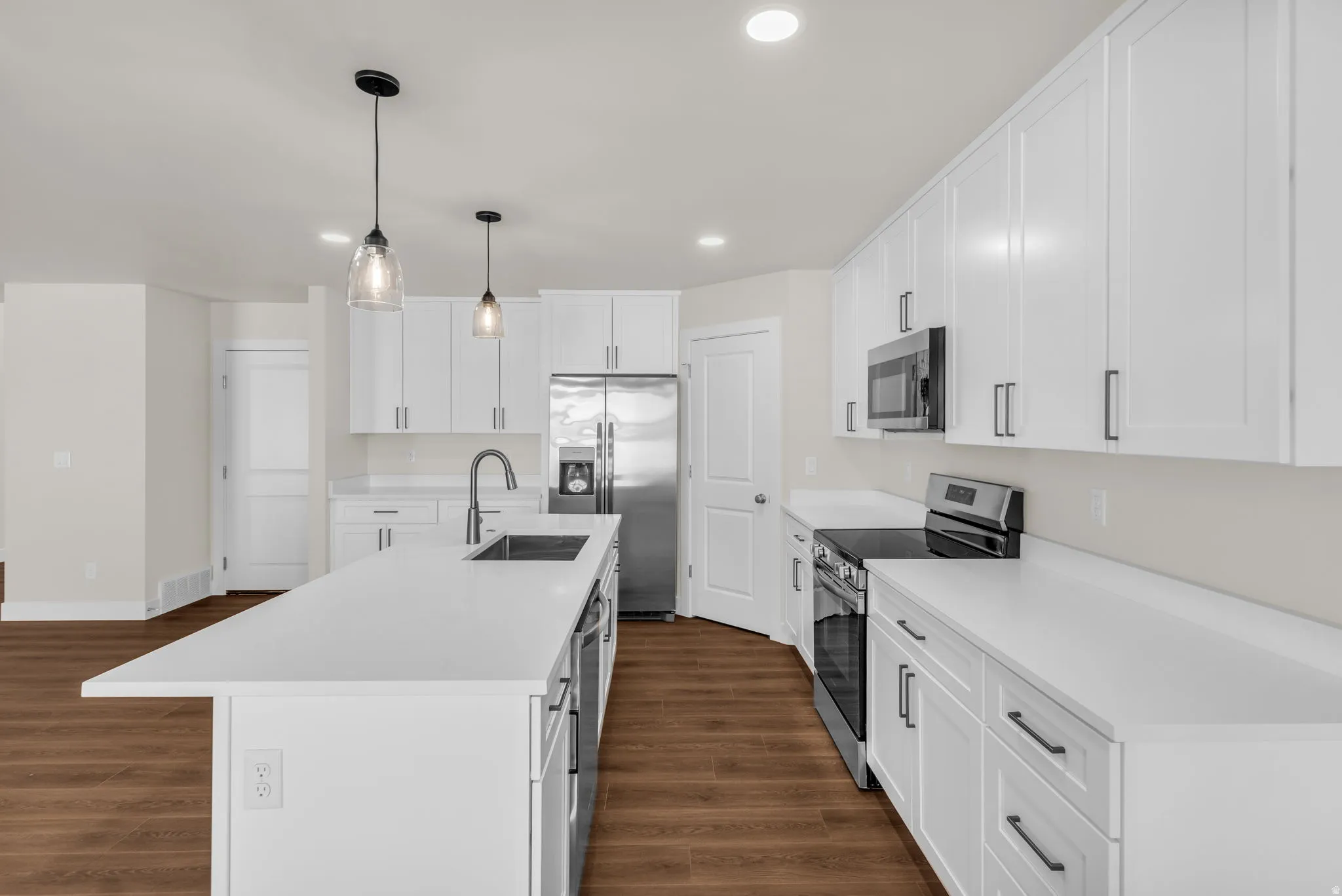 Kitchen featuring stainless steel appliances, white cabinets, pendant lighting, and a center island with sink
