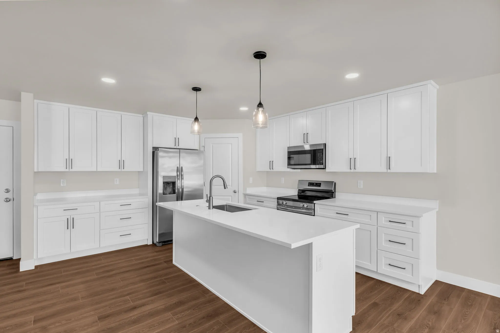 Kitchen featuring stainless steel appliances, a kitchen island with sink, hanging light fixtures, white cabinets, and dark wood-style flooring