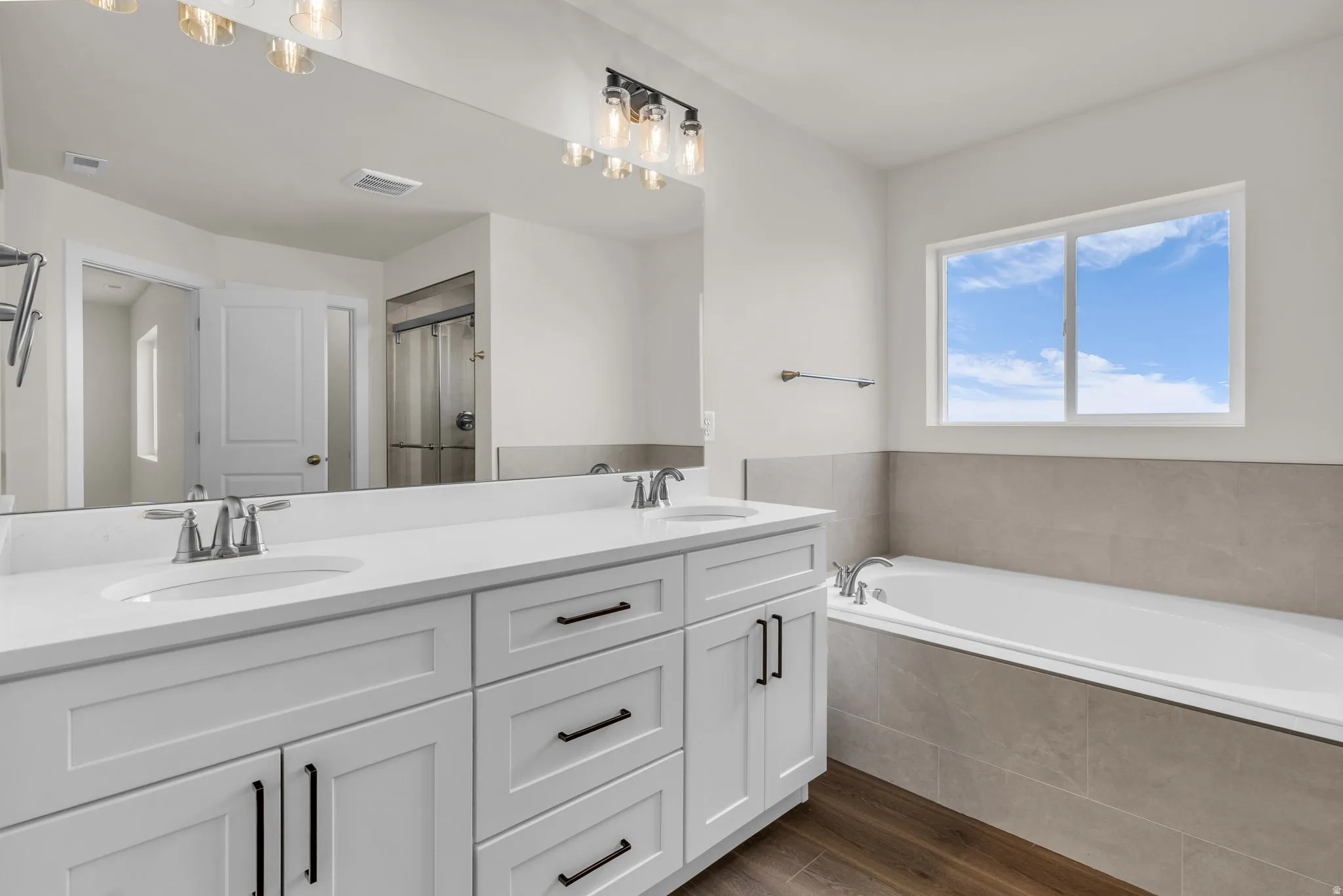 Bathroom featuring dark wood-type flooring, double vanity, a garden tub, and a shower with curtain