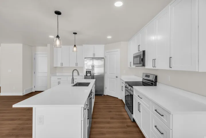 Kitchen featuring stainless steel appliances, white cabinets, pendant lighting, and a center island with sink