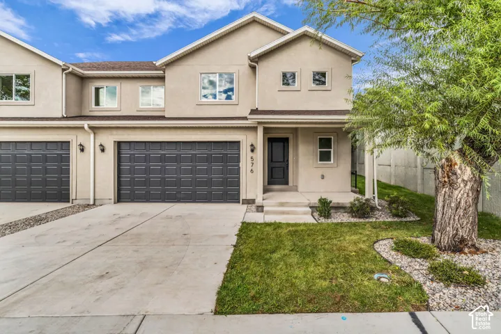 Stucco exterior featuring dual garage doors, a concrete driveway, and a front entry with adjacent landscaping