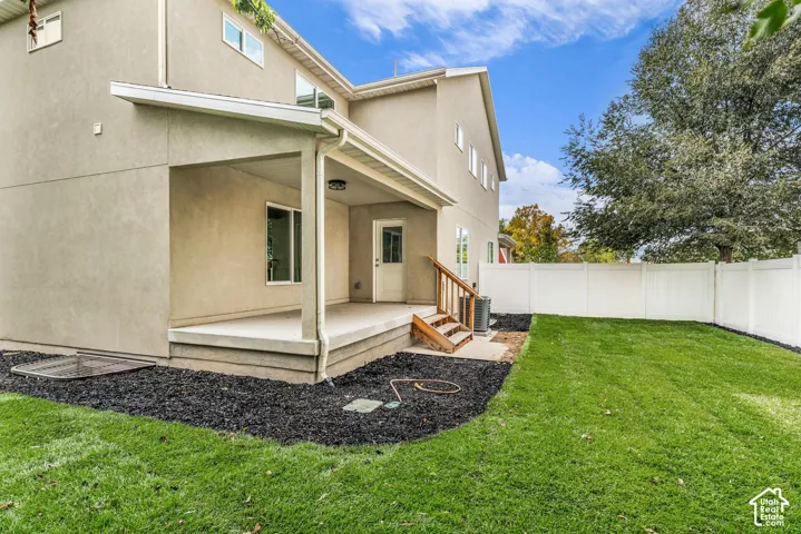 Covered patio with concrete flooring, private yard with green lawn, and full white privacy fencing