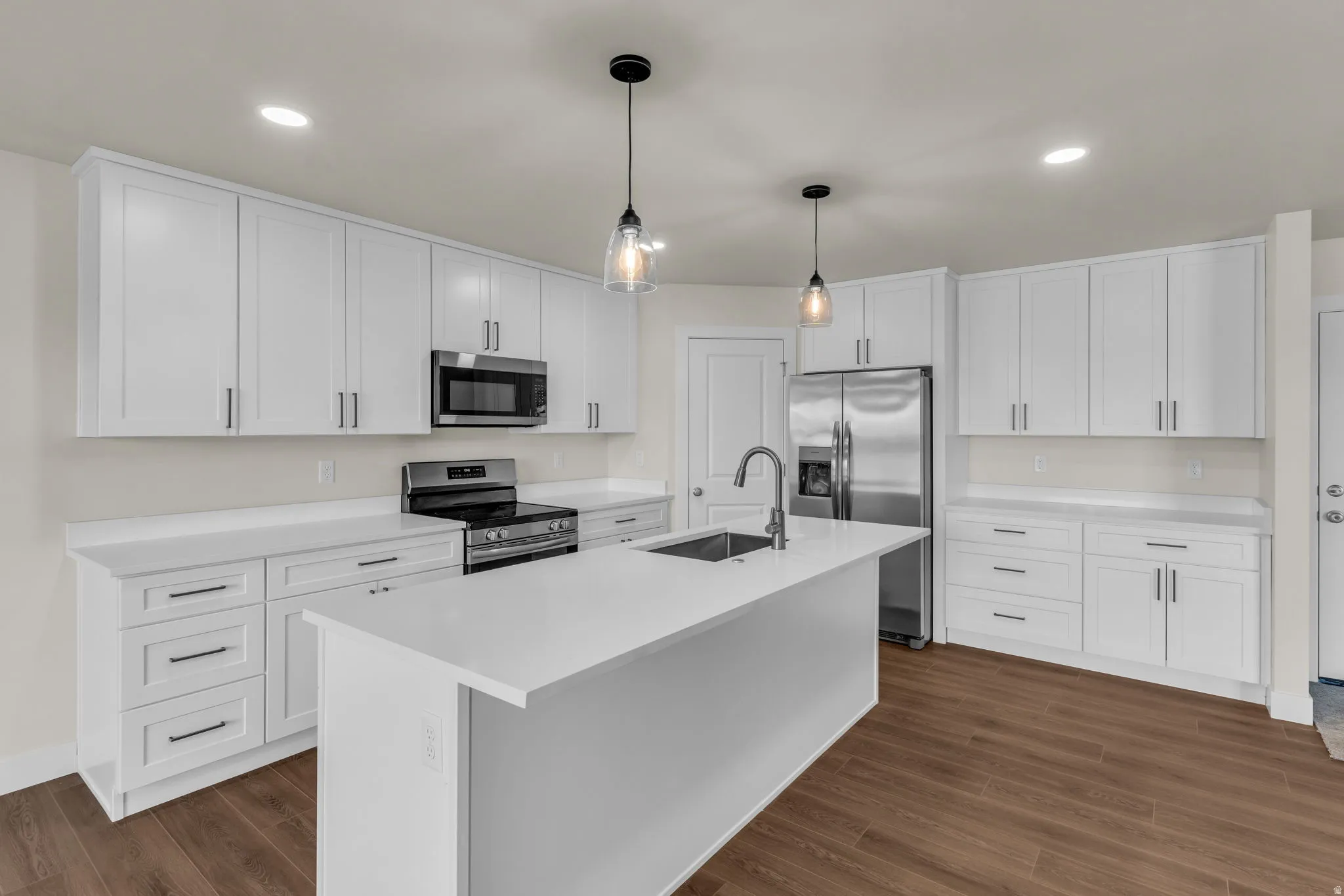 Kitchen featuring stainless steel appliances, white cabinetry, hanging light fixtures, and an island with sink