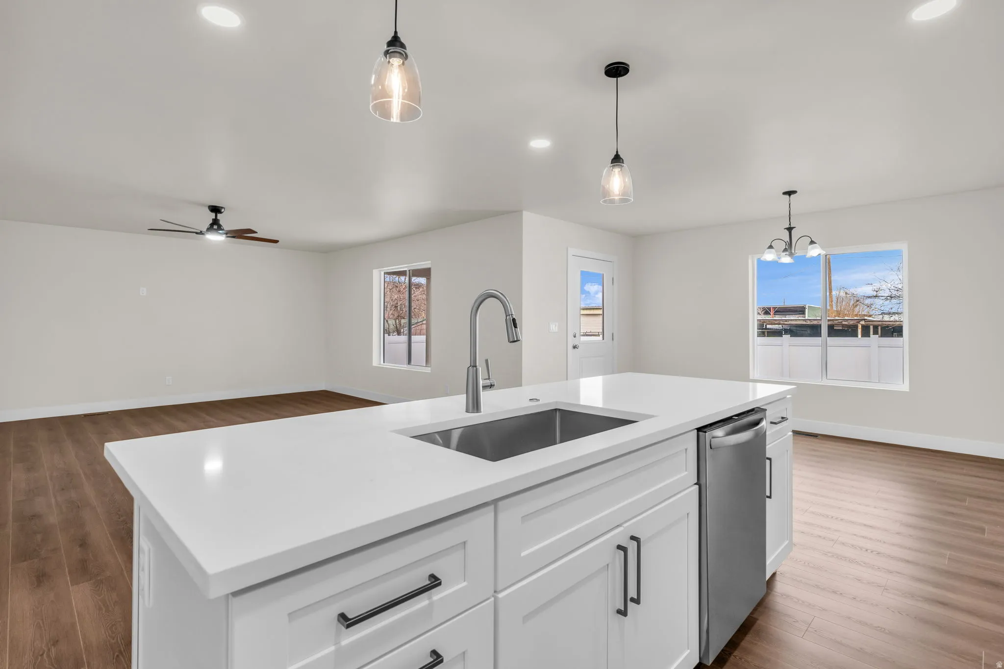 Kitchen featuring dark wood-style floors, white cabinets, stainless steel dishwasher, open floor plan, and an island with sink