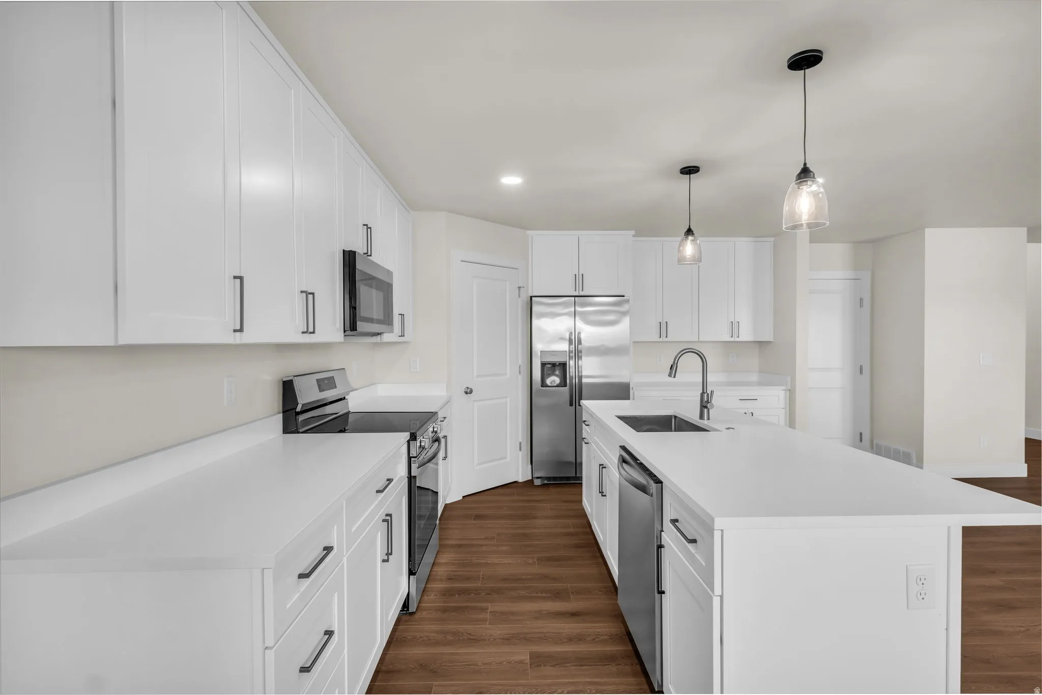 Kitchen with stainless steel appliances, white cabinetry, dark wood finished floors, and a center island with sink