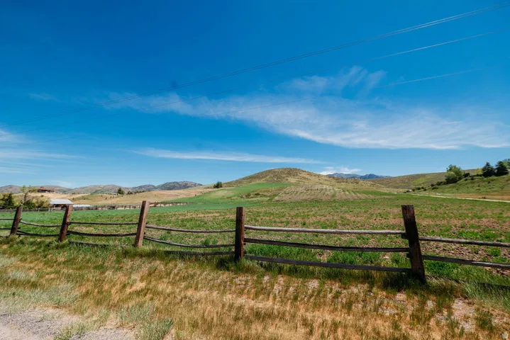 Expansive rural landscape featuring a wooden split-rail fence, rolling hills, and green fields