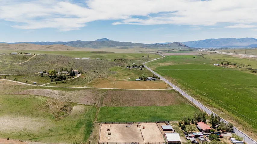 Expansive rural landscape featuring a paved road, agricultural fields, and distant mountain ranges under a clear sky