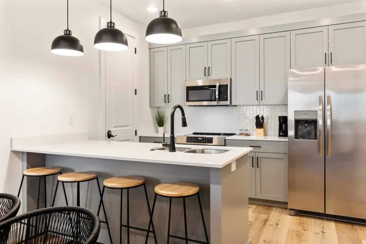 Kitchen featuring stainless steel appliances, gray cabinets, a peninsula, a breakfast bar, and hanging light fixtures
