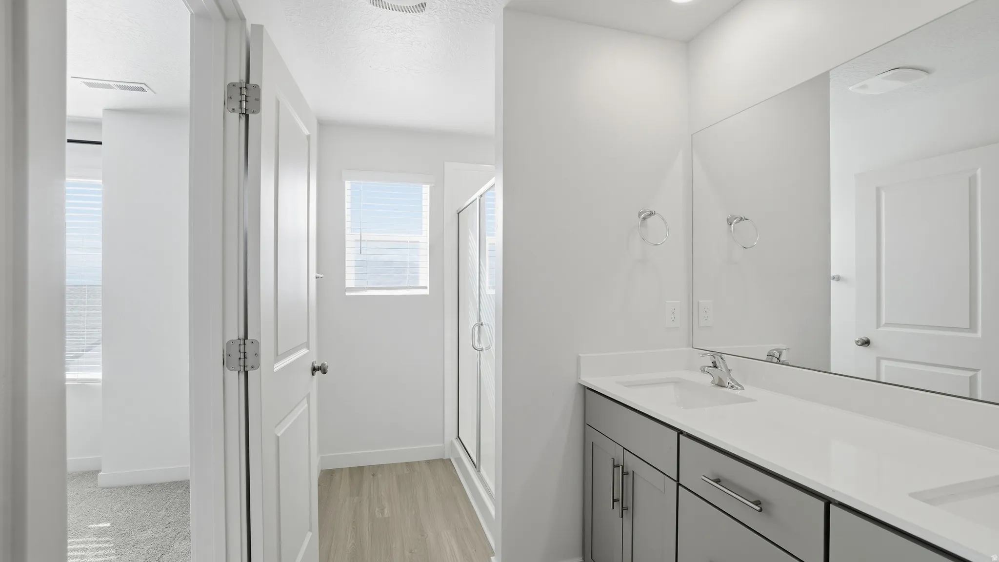 Full bath featuring double vanity, a shower stall, a textured ceiling, and light wood finished floors