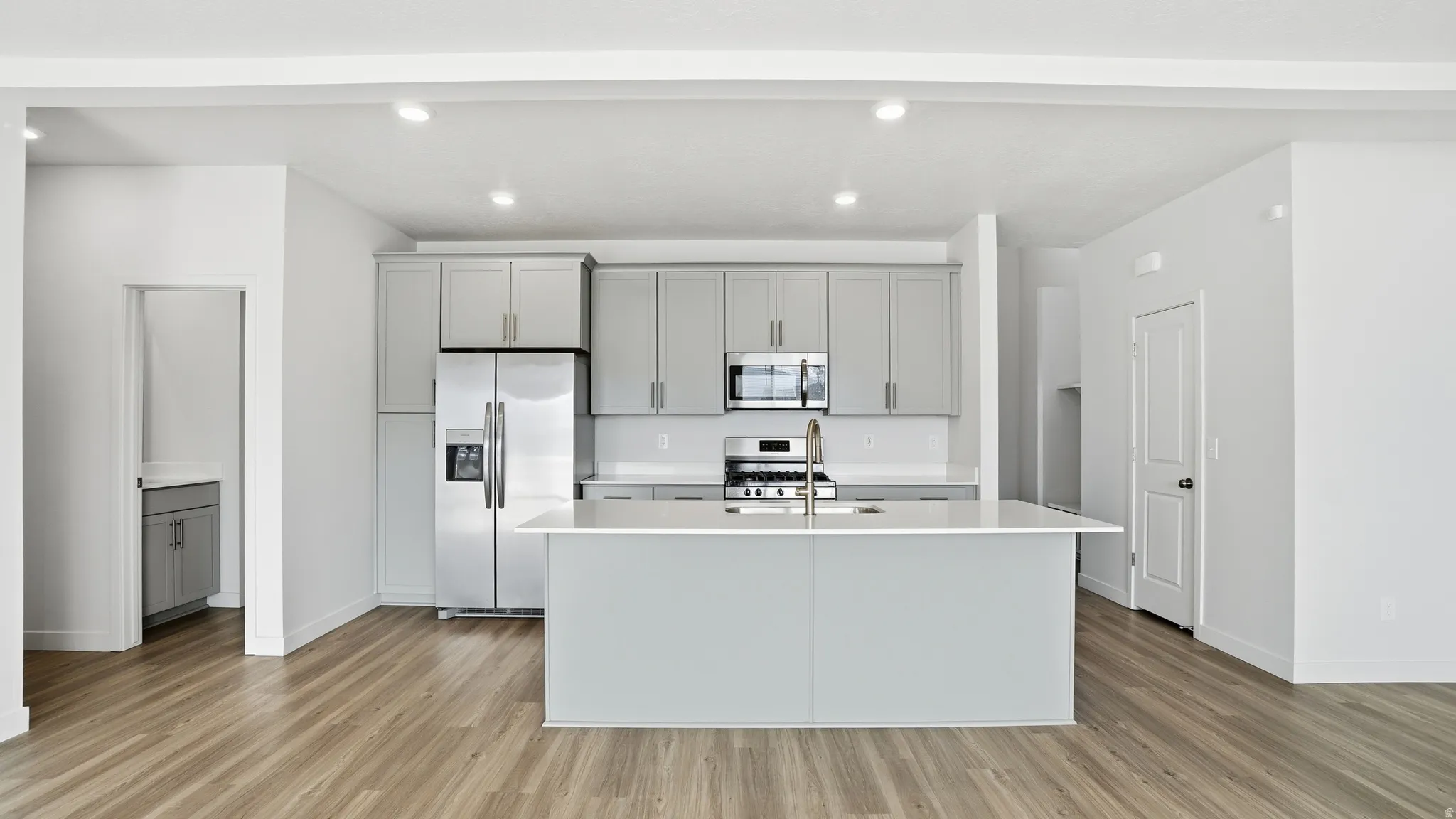 Kitchen featuring gray cabinetry, stainless steel appliances, an island with sink, light wood finished floors, and recessed lighting
