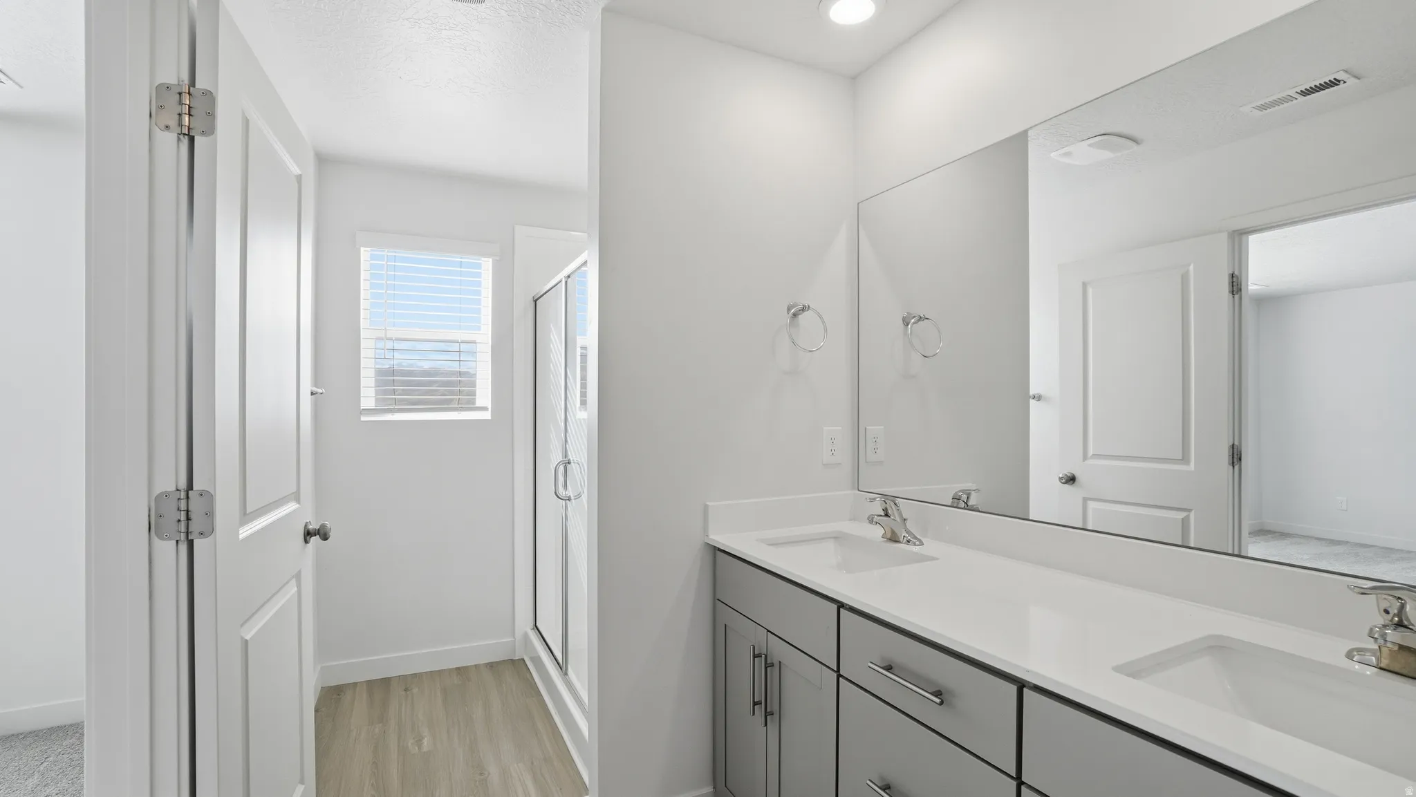 Full bath featuring a stall shower, double vanity, light wood-type flooring, and a textured ceiling