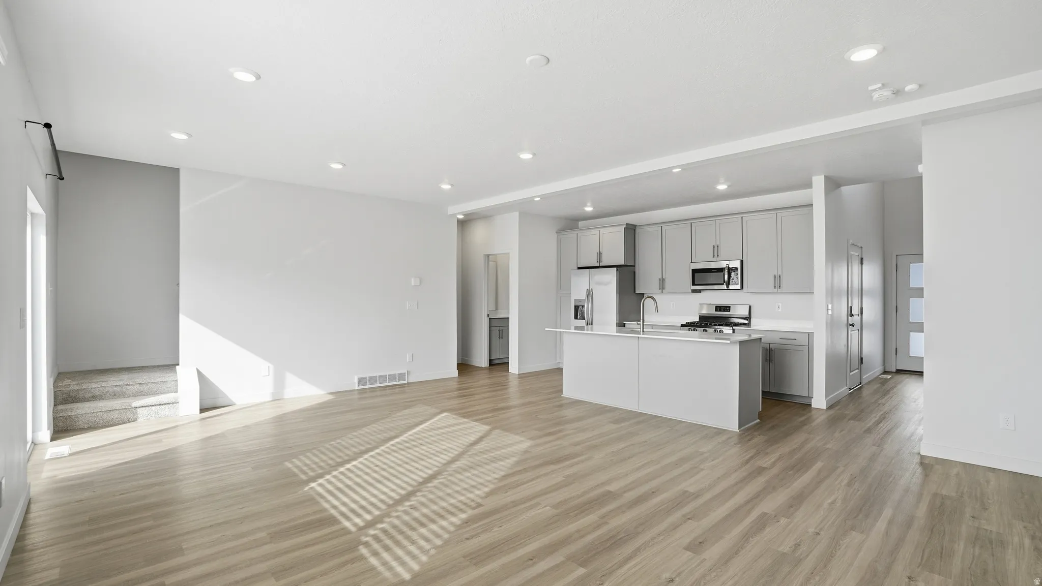 Kitchen featuring open floor plan, gray cabinetry, a kitchen island with sink, recessed lighting, and light wood-style floors
