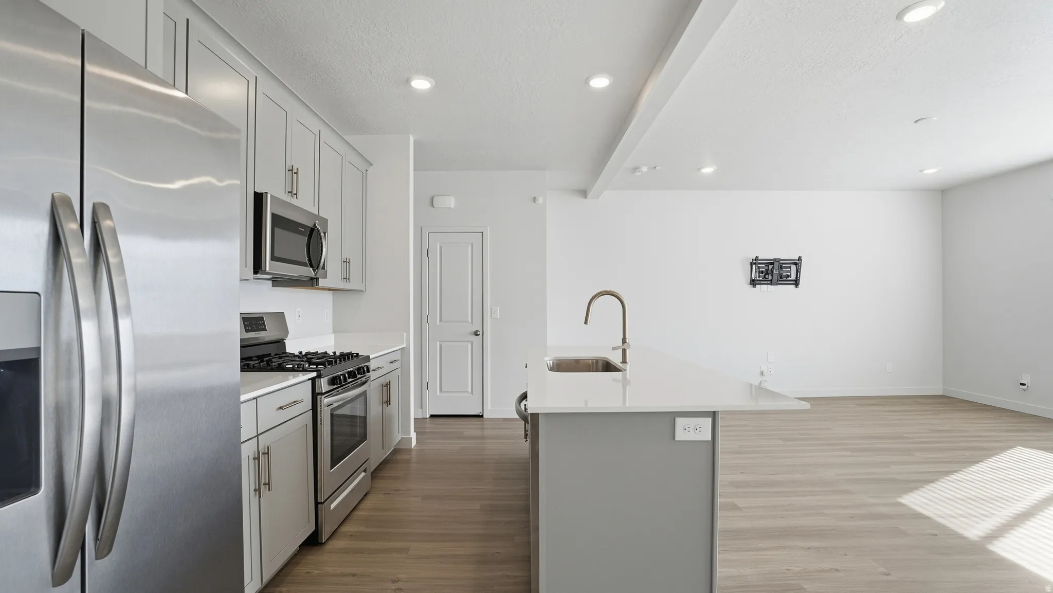 Kitchen featuring stainless steel appliances, gray cabinets, dark wood-style flooring, a kitchen island with sink, and recessed lighting