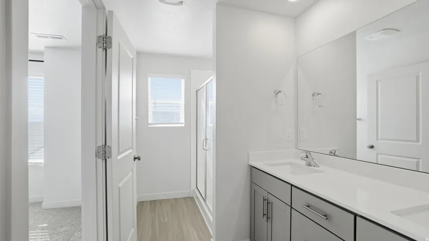 Full bath featuring double vanity, a shower stall, a textured ceiling, and light wood finished floors