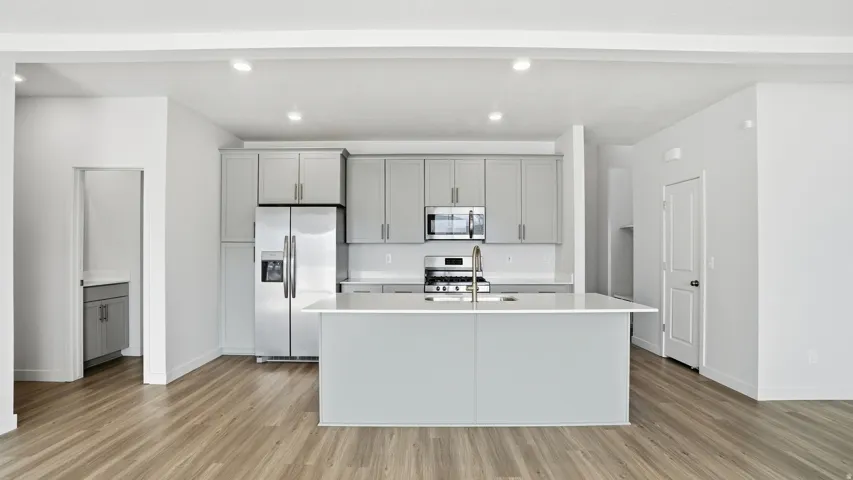 Kitchen featuring gray cabinetry, stainless steel appliances, an island with sink, light wood finished floors, and recessed lighting