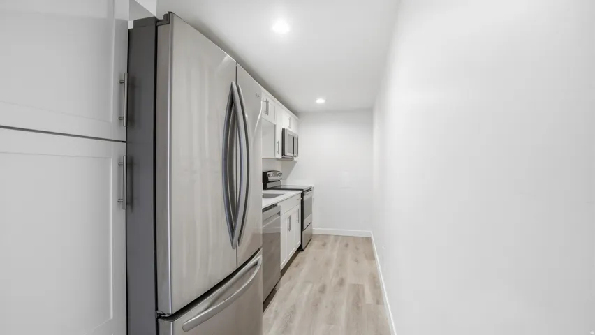 Kitchen featuring stainless steel appliances, white cabinets, light wood-type flooring, light countertops, and recessed lighting