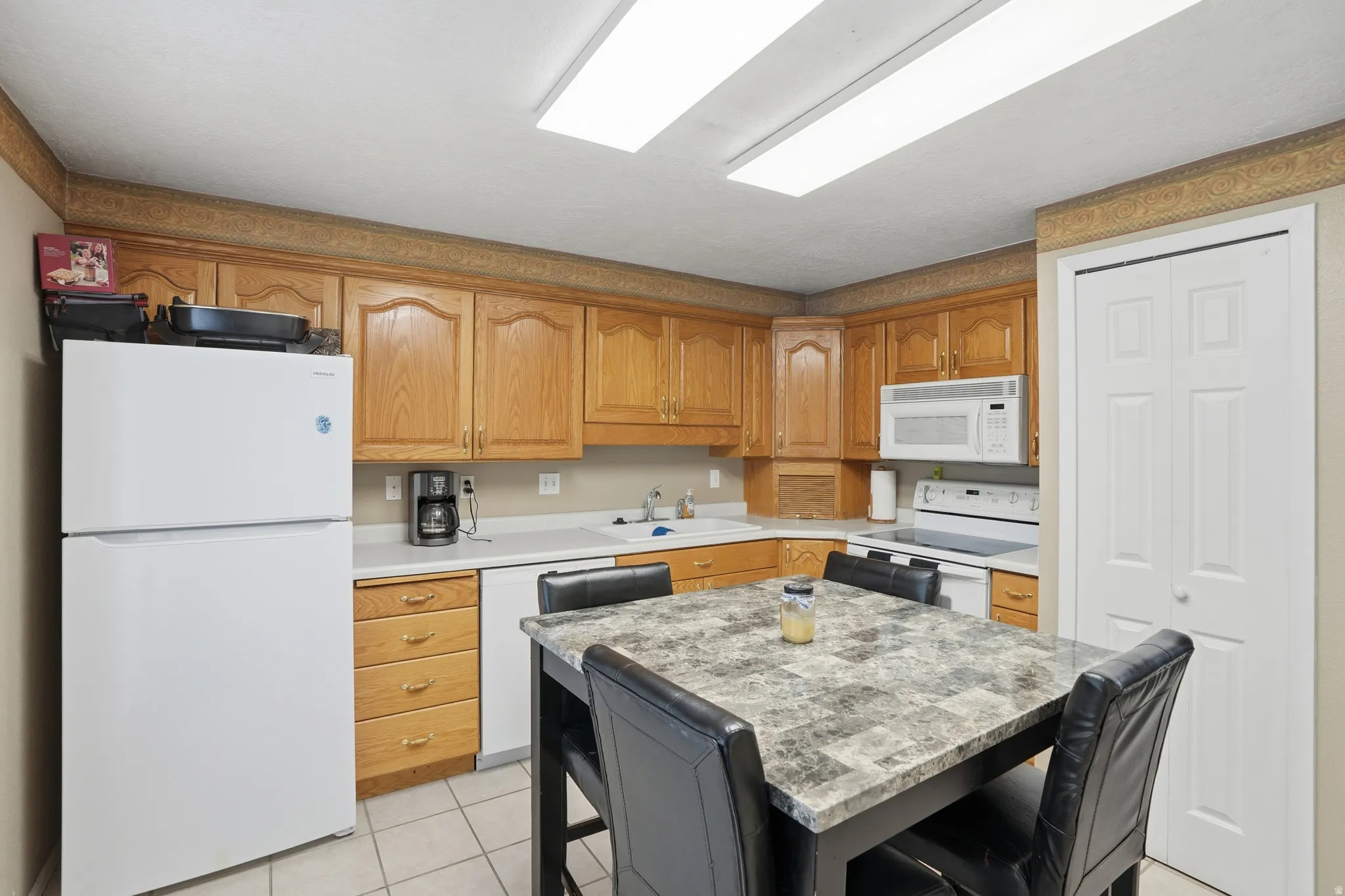 Kitchen featuring white appliances, light countertops, light tile patterned flooring, and a kitchen island