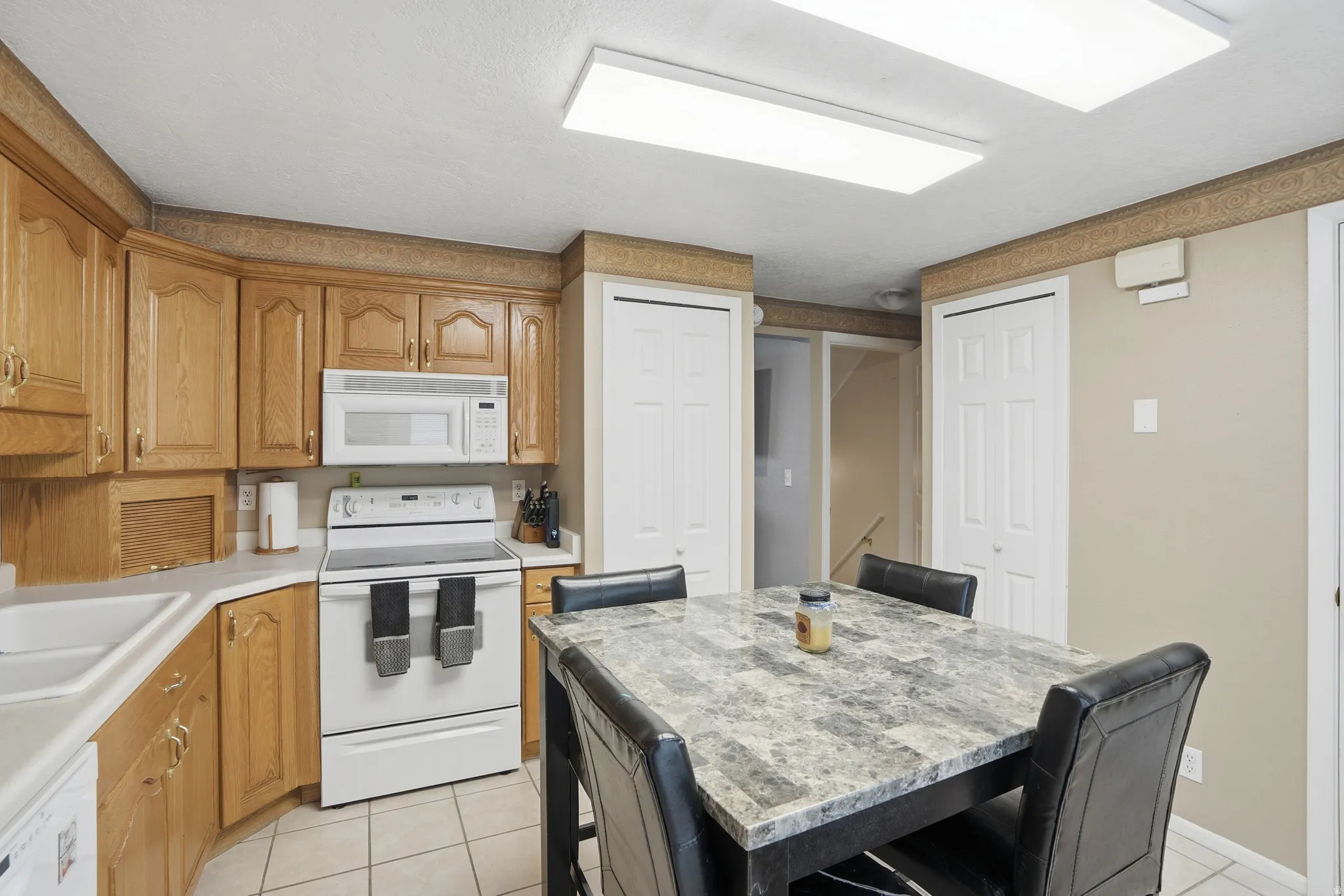 Kitchen featuring white appliances, light countertops, light tile patterned floors, and wood finish cabinets