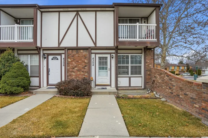 View of front of property with brick siding, a front lawn, a balcony, and stucco siding