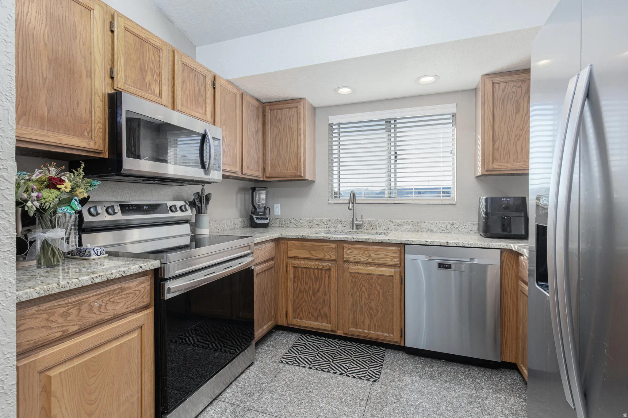 Kitchen with stainless steel appliances, light stone counters, recessed lighting, and granite tiled floors