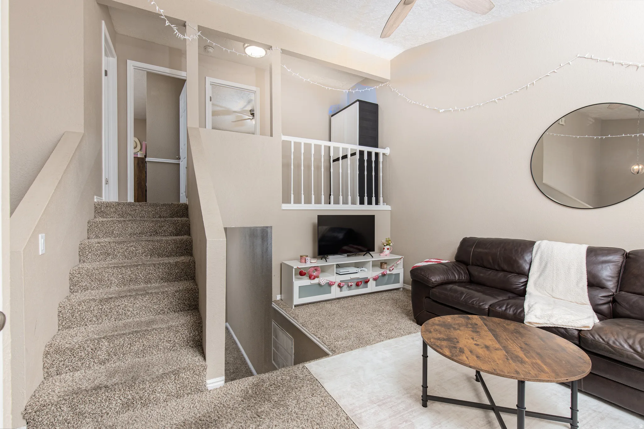 Carpeted living room featuring a ceiling fan and stairway