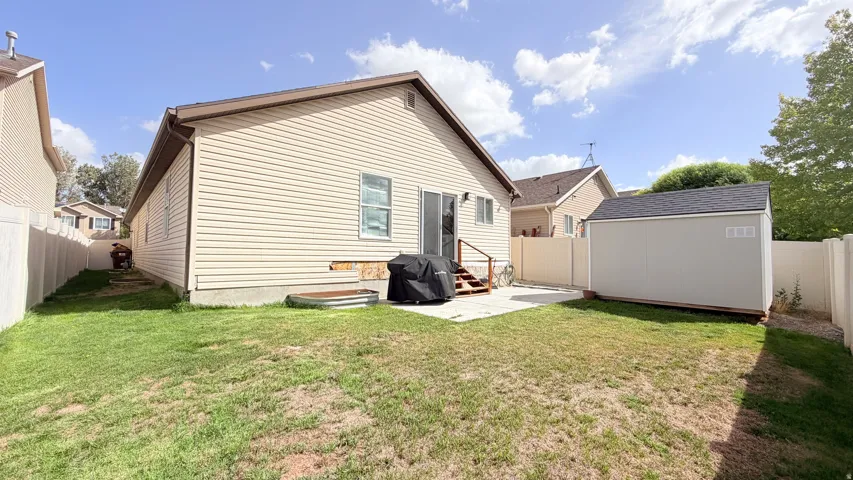 Fenced backyard featuring a concrete patio, sliding glass door, and a detached storage shed with a shingle roof