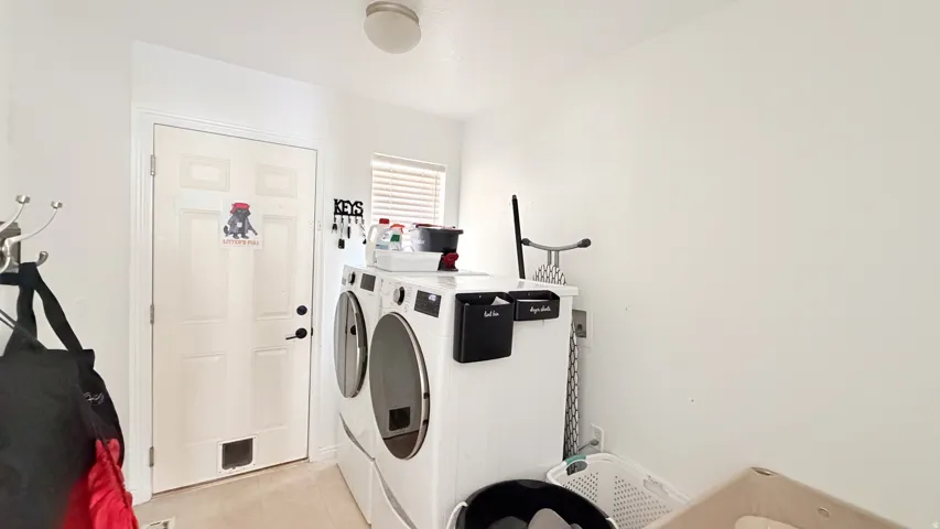 White paneled door with dark hardware, front-loading washer and dryer, and a single window with blinds