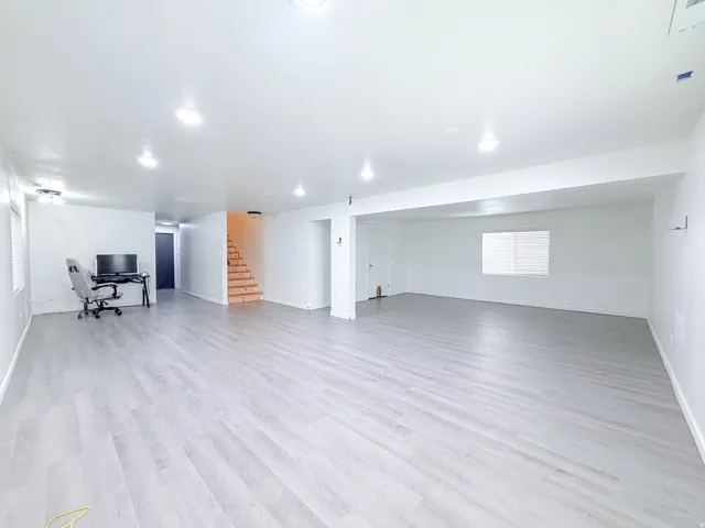 Expansive open-concept living area featuring light wood-finish flooring, recessed lighting, and a staircase with natural wood treads