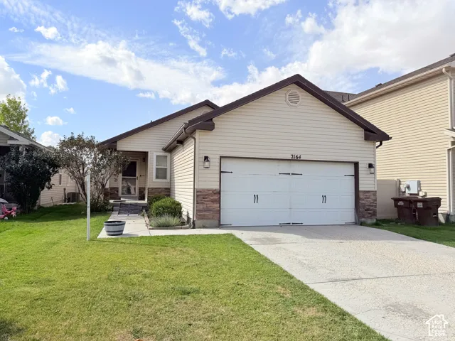 Siding exterior with stone veneer accents, attached garage with decorative hardware, concrete driveway, and covered entry