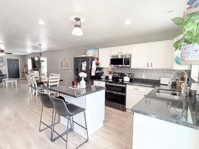 Kitchen featuring white cabinetry, dark stone-finish countertops, stainless steel appliances, and wood-finish flooring