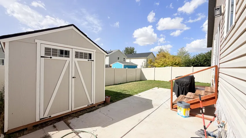 Backyard featuring a concrete patio, a wooden shed with double doors, and a partial deck with railing