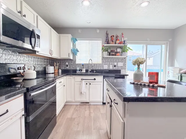 White cabinetry, black countertops, stainless steel appliances, wood-finish flooring, and a sliding glass door
